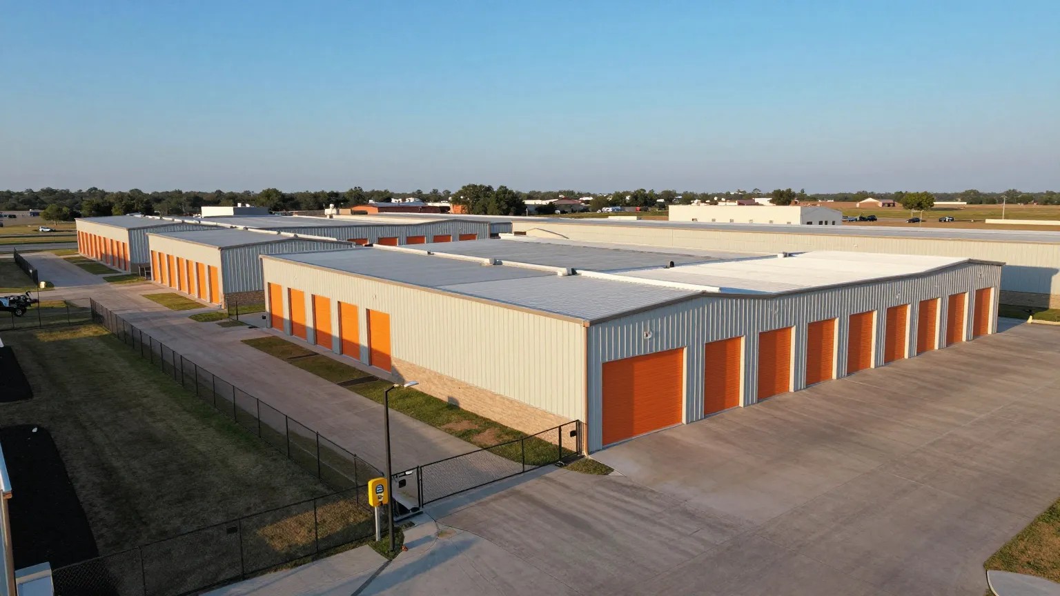 Aerial view of a fenced, gated self-storage facility with rows of orange roll-up doors